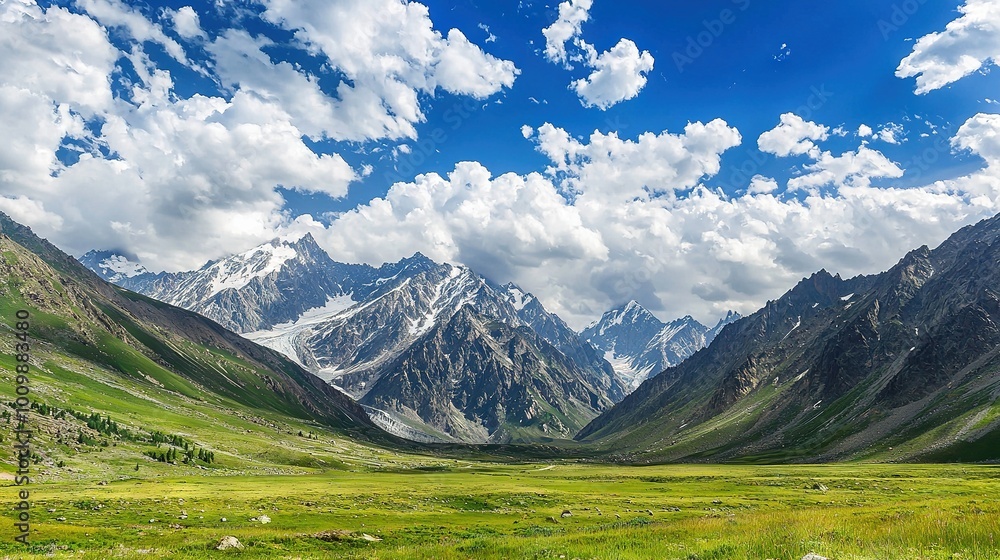 A valley surrounded by mountains under a blue sky with white clouds and lush green grass in the foreground A valley surrounded by mountains under a blue sky with white clouds and lush green grass in the foreground