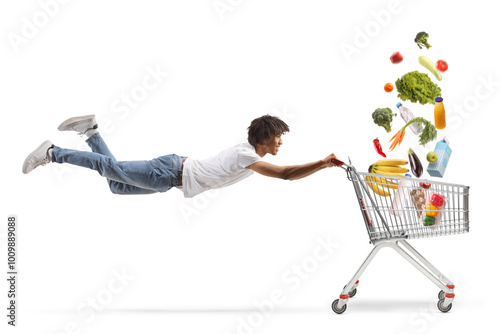 African american guy flying and holding a shopping cart with groceries falling inside photo