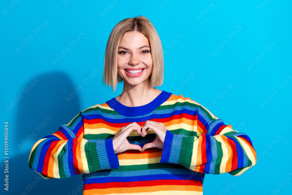 Portrait of pretty young girl show heart symbol wear striped pullover isolated on blue color background Portrait of pretty young girl show heart symbol wear striped pullover isolated on blue color background