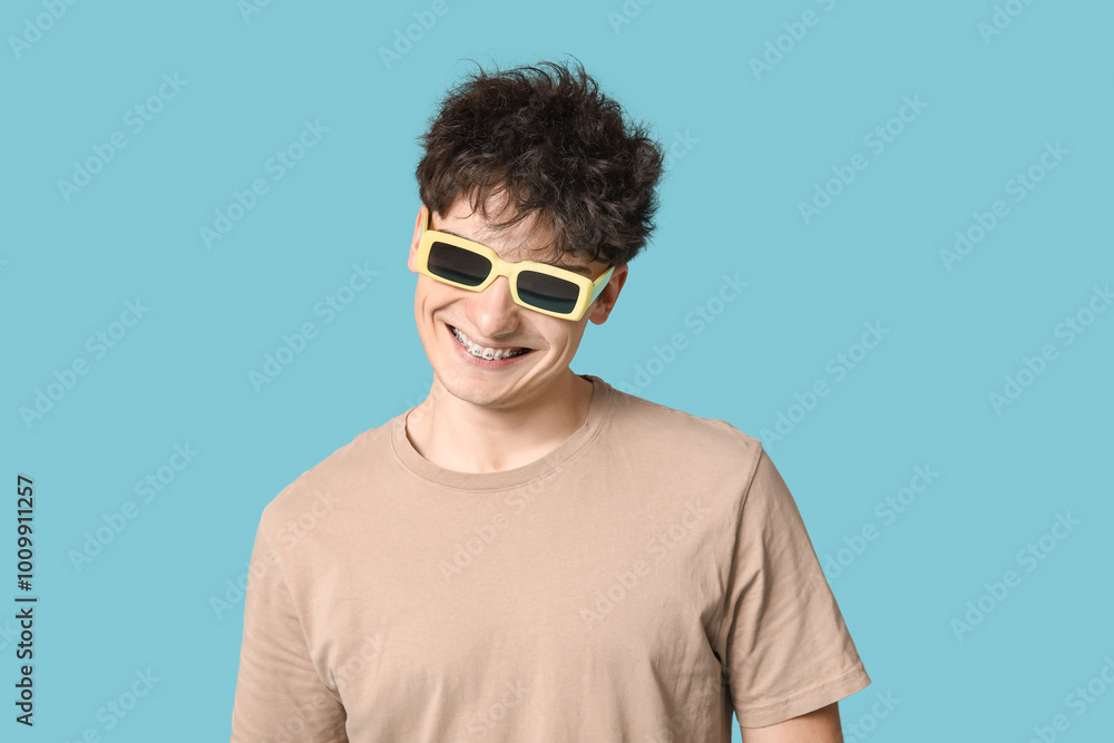 Handsome young man in stylish beige t-shirt and sunglasses on blue background Handsome young man in stylish beige t-shirt and sunglasses on blue background