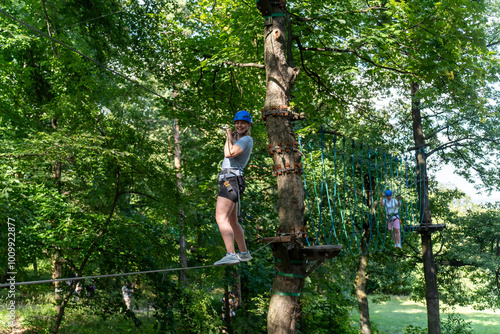 Woman in helmet walking on rope bridge during obstacle course in the forest, balancing. Concept of outdoor adventure, physical activity, and overcoming challenges in nature.