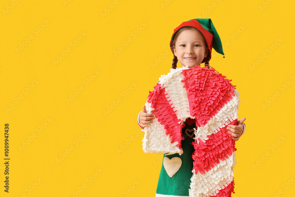 Cute little girl in elf costume with candy cane pinata on yellow background Cute little girl in elf costume with candy cane pinata on yellow background