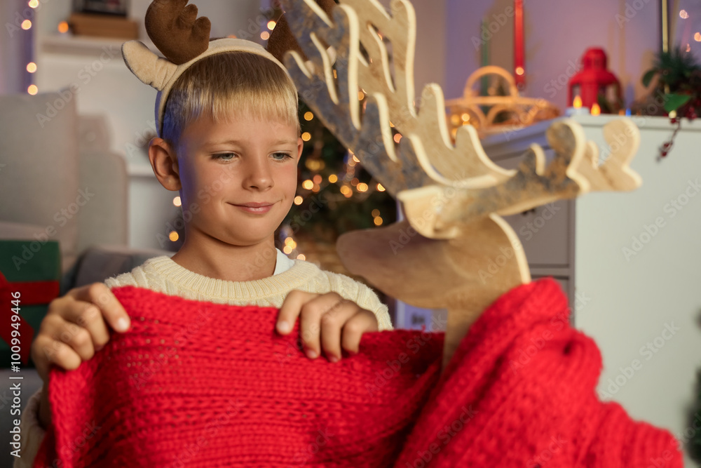 Φωτογραφία Little boy wrapping wooden reindeer with scarf at home on Christmas eve, closeup