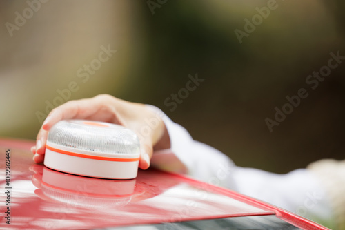 Young woman with reflective vest, places the V16 emergency light beacon on the roof of the damaged vehicle. Help flash, mandatory to replace triangles in Europe. DGT Spain.