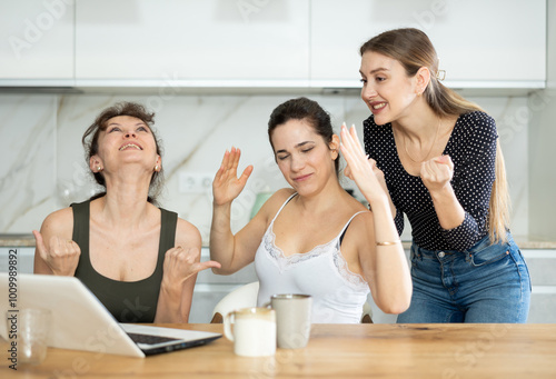 Joyful middle-aged women gloating over having won a prize sitting at notebook in the kitchen photo