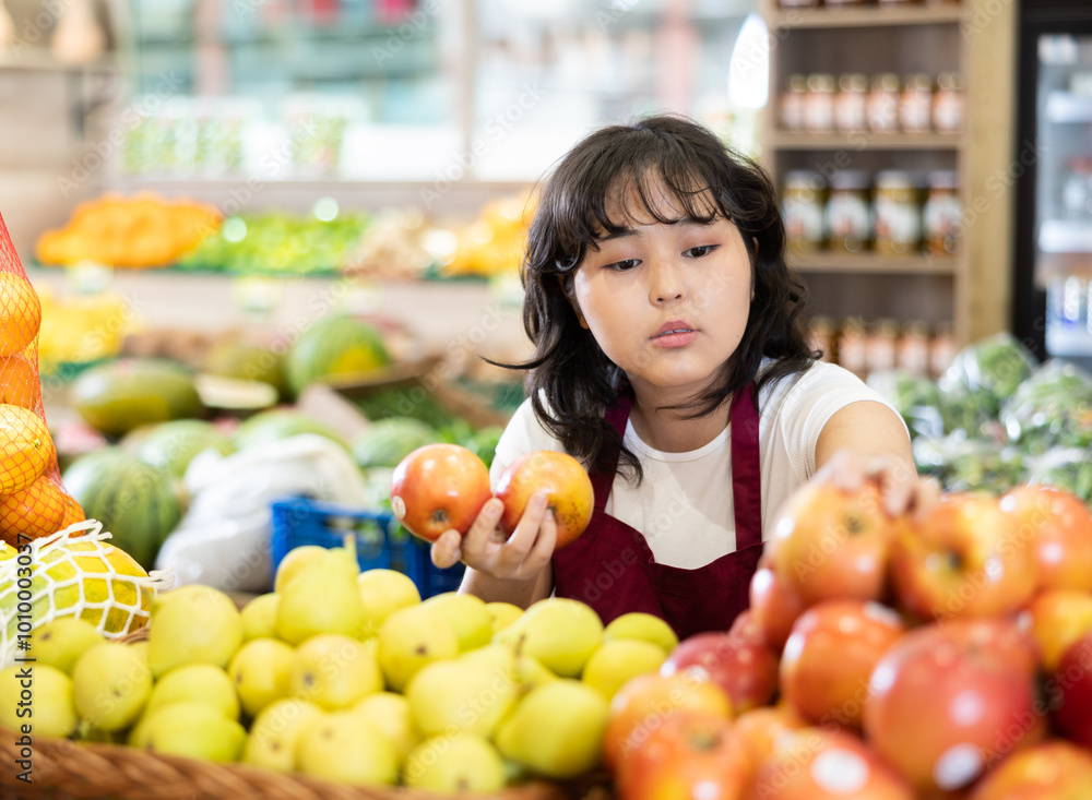 Φωτογραφία Young asian girl in apron working at farmers market, arranging ripe apples on produce display with fruits and vegetables
