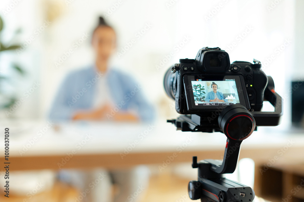 On a camera screen pretty indian or arabian brunette young woman, blogger, influencer sits at a desk, looking at camera, recording education tutorial vlog, video course for social media On a camera screen pretty indian or arabian brunette young woman, blogger, influencer sits at a desk, looking at camera, recording education tutorial vlog, video course for social media