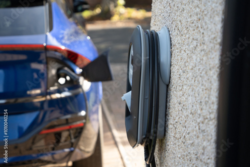 A blue Electric car charging on a home charger on a sunny day