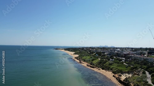 Aerial drone footage of the Melbourne skyline viewed from Sandringham Beach, showcasing the stunning contrast between the sandy shore and the bustling cityscape, highlighting the beauty of coastal Mel