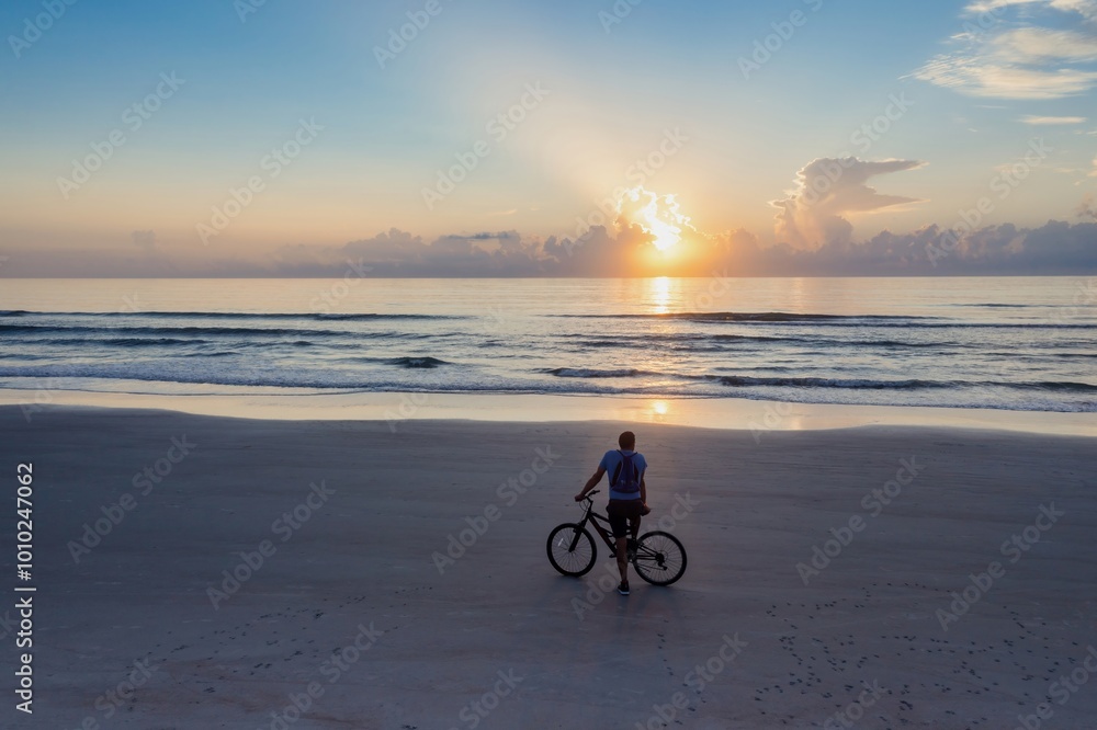 Fototapeta premium Man on a bicycle on a beach looking out to the sunrise, Daytona Beach, Florida, United States.
