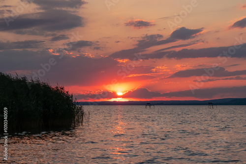 Fiery sunset over calm lake Balaton, Hungary, Europe. Dramatic sky is ablaze with vibrant hues of orange and red. Tranquility, natural beauty. Peaceful mesmerizing lakeside scene. Romantic landscape photo