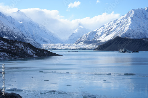 Majestic snow-capped mountains towering over a tranquil lake filled with floating ice in New Zealand. The vast landscape offers a breathtaking view of nature’s raw beauty.