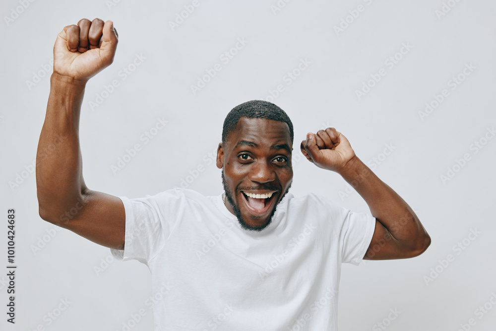 Happy man celebrating success with raised arms wearing a white shirt against a plain light background His joyful expression conveys excitement and positivity Happy man celebrating success with raised arms wearing a white shirt against a plain light background His joyful expression conveys excitement and positivity