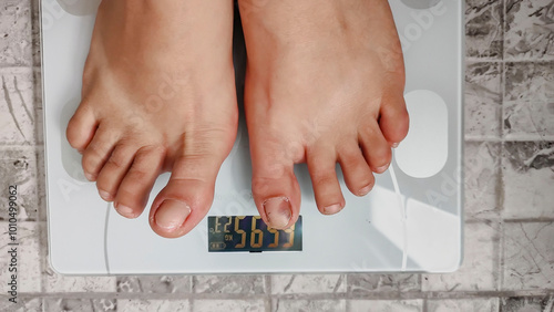 Close-up of woman's feet on digital scale, concept of weight in home environment. Woman standing barefoot on scale, weighing over 66 kilos.