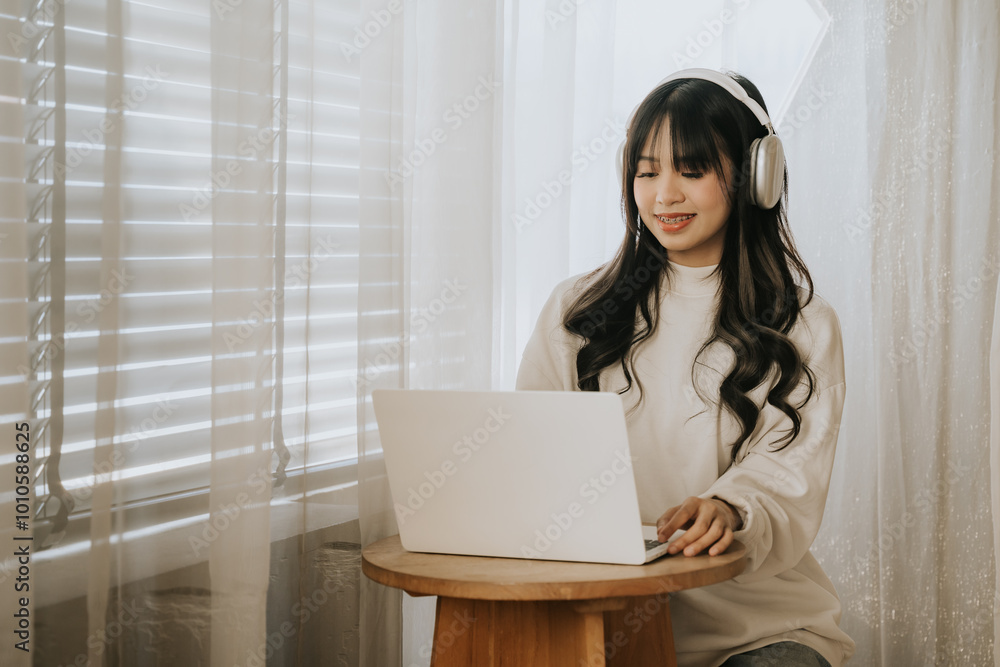 Focused Work from Home: A young woman with headphones on, engrossed in work on her laptop, bathed in natural light streaming through a window. Focused Work from Home: A young woman with headphones on, engrossed in work on her laptop, bathed in natural light streaming through a window.