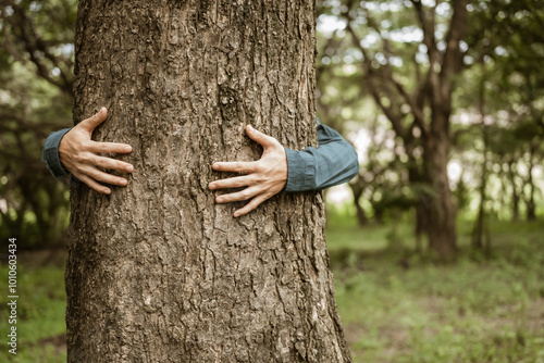 A male hand hugs a tree, symbolizing love for nature and the environment. This act represents the importance of trees in preventing global warming and restoring environmental balance, as seen