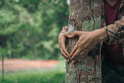 A male hand hugs a tree, symbolizing love for nature and the environment. This act represents the importance of trees in preventing global warming and restoring environmental balance, as seen