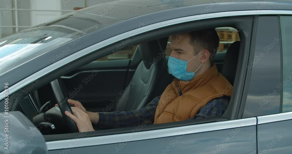 Man in car with surgical mask on face against Coronavirus Disease 2019. COVID-19 Pandemic Coronavirus. Man in car with surgical mask on face against Coronavirus Disease 2019. COVID-19 Pandemic Coronavirus.