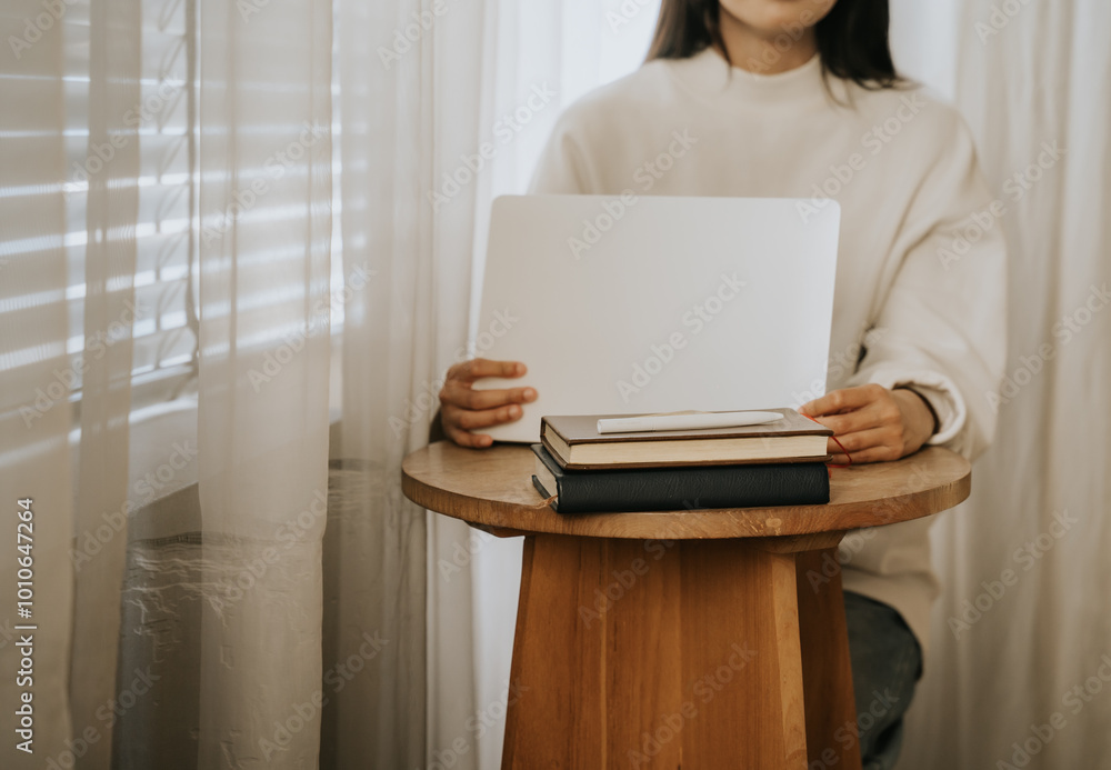 Cozy Study Session: A woman gently holds a blank sketchbook, surrounded by books on a minimalist wooden table, bathed in soft natural light from a nearby window. Perfect for educational, artistic. Cozy Study Session: A woman gently holds a blank sketchbook, surrounded by books on a minimalist wooden table, bathed in soft natural light from a nearby window. Perfect for educational, artistic.