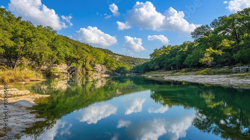 A peaceful scene of a cool blue sky with fluffy white clouds reflected in a calm river, surrounded by trees.