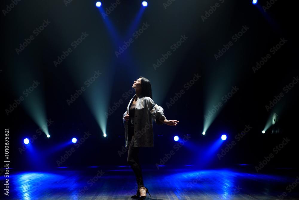 Fototapeta premium Girl in black suit performing on stage with bright blue background