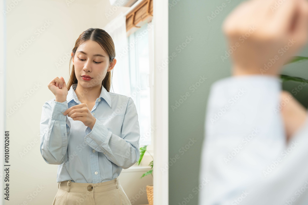 Get dress, pretty asian young woman, businesswoman standing wearing striped shirt, female getting dressed preparing before go to work looking reflection in the mirror in the morning at home. Get dress, pretty asian young woman, businesswoman standing wearing striped shirt, female getting dressed preparing before go to work looking reflection in the mirror in the morning at home.
