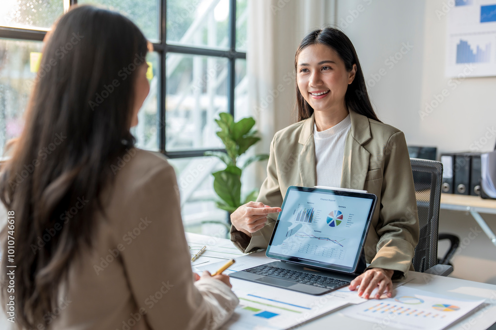 Businesswoman pointing at tablet showing financial chart to colleague Businesswoman pointing at tablet showing financial chart to colleague