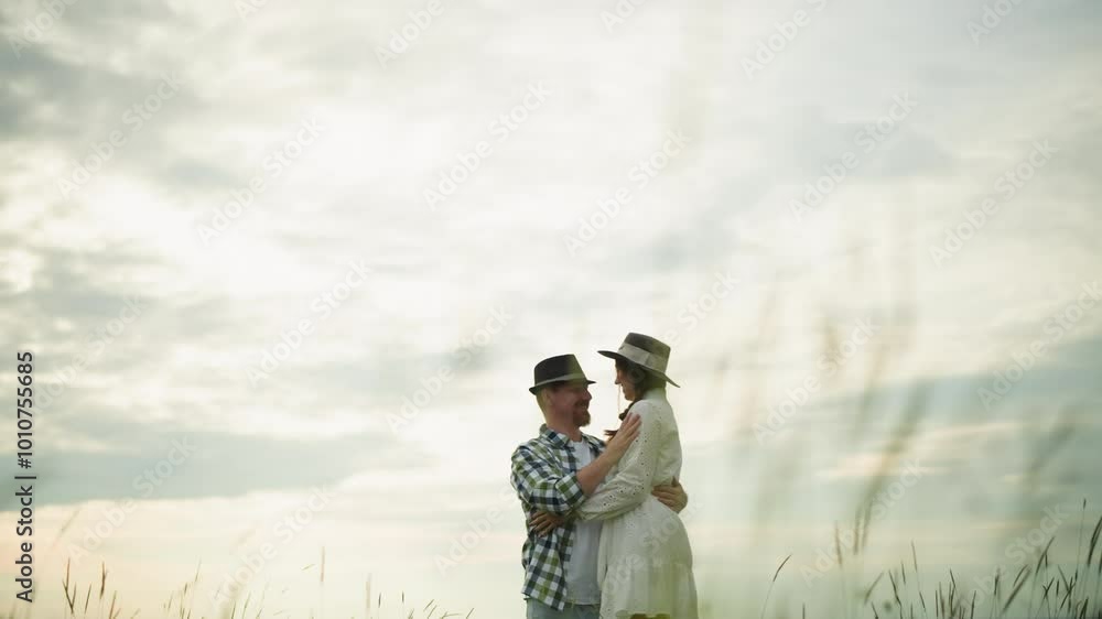 custom made wallpaper toronto digitalA joyful couple embraces in a grassy field, both wearing hats. The woman is dressed in a white dress, and the man in a checkered shirt. The scene captures their happiness and love in a serene