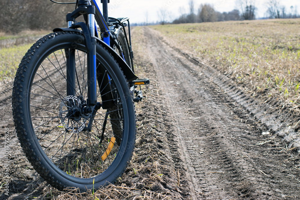 Fototapeta premium front wheel of a mountain bike. Mountain bike. stands on a field road. concept of cycling, repair or breakage, sports, outdoor activities. bike on trail, front wheel in focus. space for text