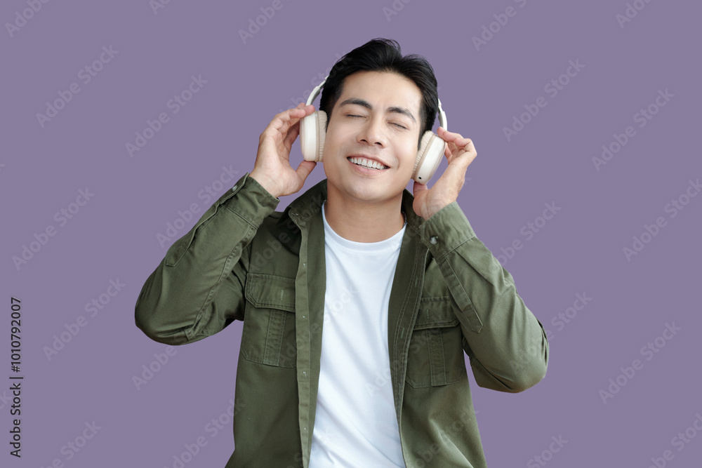 Young guy in wireless headphones enjoying the music against purple background Young guy in wireless headphones enjoying the music against purple background