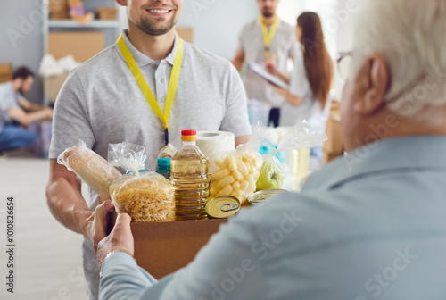 A smiling volunteer guy gives an elderly man a box of groceries. Concept of care for the elderly, support for migrants. Adaptation to new living conditions, pension provision,  photo