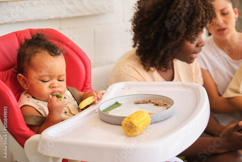 Multiracial family at mealtime: baby eating, women interacting photo