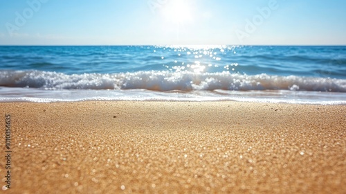 Fine beach sand in the foreground, leading to the gently rolling waves of the sea in the background under the bright summer sun. Ideal for a coastal vacation scene.