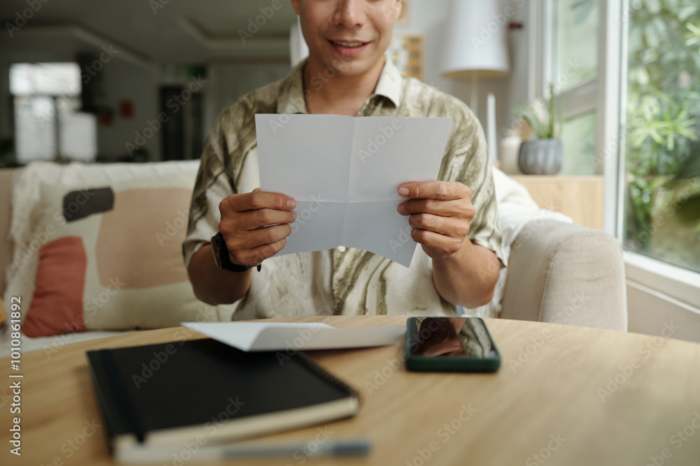 Smiling man sitting on sofa in the living room and reading letter Smiling man sitting on sofa in the living room and reading letter