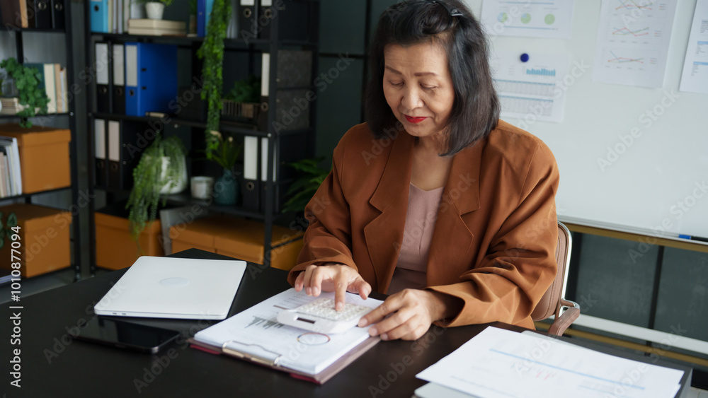 Middle age Asian woman Auditor or internal revenue service staff senior business woman checking annual financial elderly woman pressing calculator Middle age Asian woman Auditor or internal revenue service staff senior business woman checking annual financial elderly woman pressing calculator
