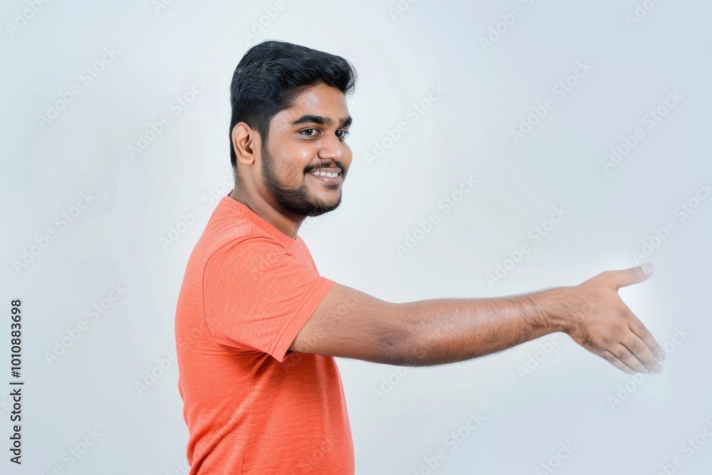 An engaging moment unfolds as a 30-year-old Indian man in an orange T-shirt reaches out with a welcoming smile, embodying friendliness and approachability in a relaxed setting. An engaging moment unfolds as a 30-year-old Indian man in an orange T-shirt reaches out with a welcoming smile, embodying friendliness and approachability in a relaxed setting.