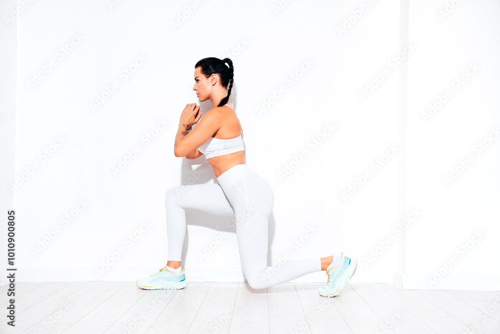 Fototapeta premium Fitness confident woman in white sports clothing. Sexy young beautiful model with perfect body. Female isolated on white wall in studio. Stretching out before training. Doing lunges