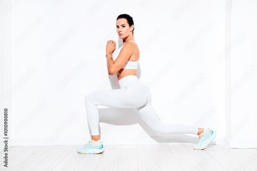 Fitness confident woman in white sports clothing. Sexy young beautiful model with perfect body. Female isolated on white wall in studio. Stretching out before training. Doing lunges Fitness confident woman in white sports clothing. Sexy young beautiful model with perfect body. Female isolated on white wall in studio. Stretching out before training. Doing lunges
