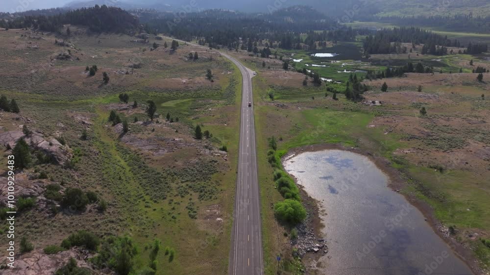 A remote road stretching through a scenic basin near a small reflective lake, aerial view A remote road stretching through a scenic basin near a small reflective lake, aerial view