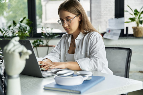 A woman sits at a desk typing on a laptop.