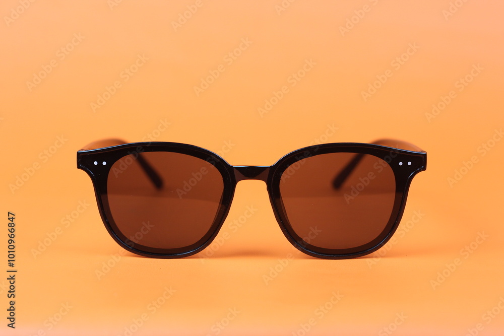 Black sunglass with oval frame, Sunglasses in beautiful fashion concept summer beach accessories. Sunglasses on orange color background. Front view