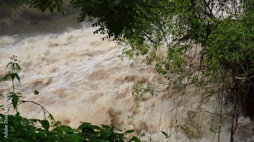 Vertical shot of a strong current near a waterfall and flash floods in a mountain river after heavy rain, showing the environmental effects of deforestation and global warming.