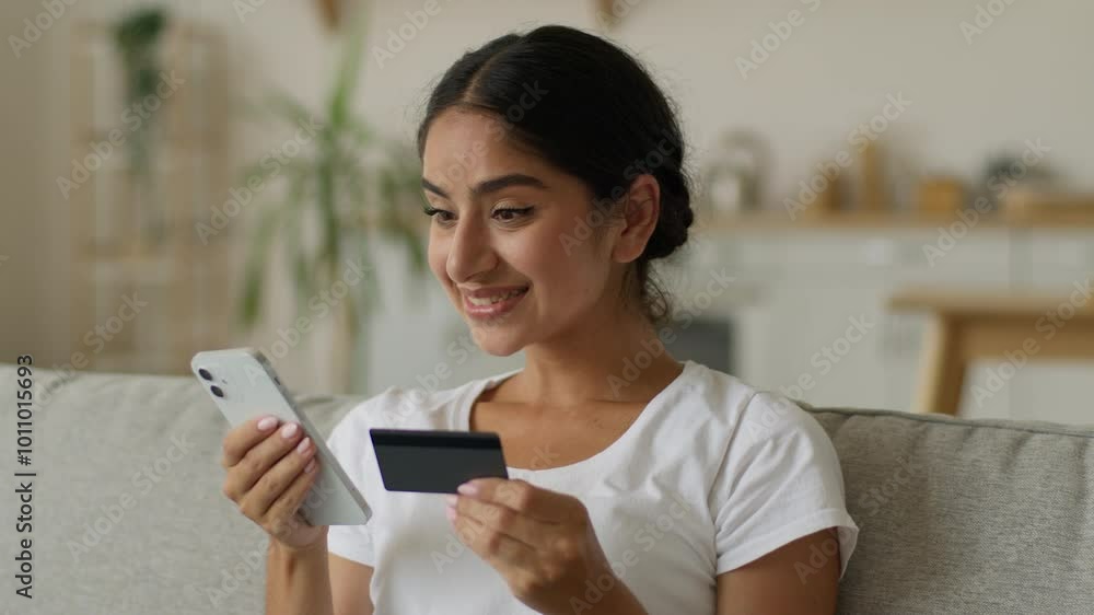 Happy smiling Indian woman buyer client Arabian girl female holding mobile phone credit bank card payment online pay enter secure number authorization buy purchase shopping internet banking at home Happy smiling Indian woman buyer client Arabian girl female holding mobile phone credit bank card payment online pay enter secure number authorization buy purchase shopping internet banking at home