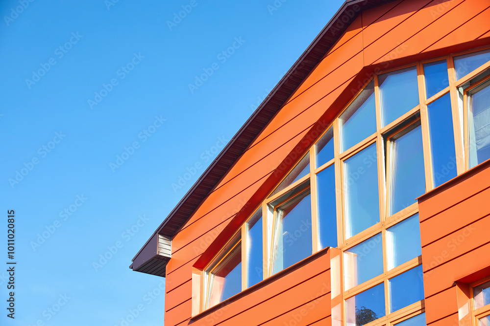 Wall of commercial building with large windows and orange metal ventilated facades made of Linear panels or facade cassettes. Fragment of building over blue sky with copyspace. Wall of commercial building with large windows and orange metal ventilated facades made of Linear panels or facade cassettes. Fragment of building over blue sky with copyspace.
