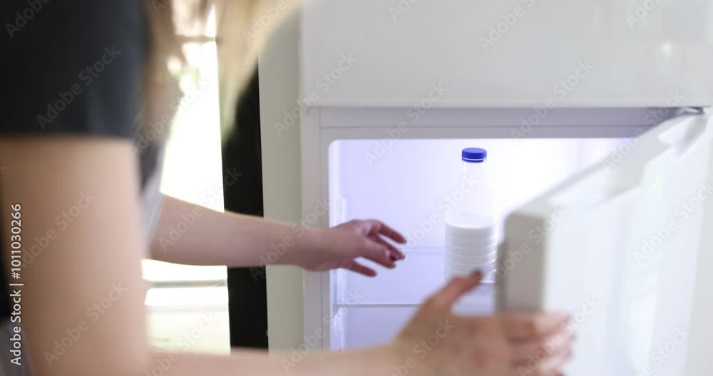 Woman opens refrigerator door and takes bottle of milk in kitchen at home Woman opens refrigerator door and takes bottle of milk in kitchen at home