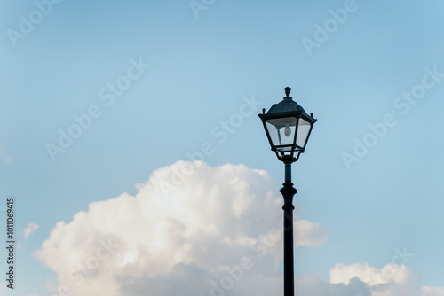 An elegant street lamp stands against a backdrop of lush clouds and a clear blue sky.