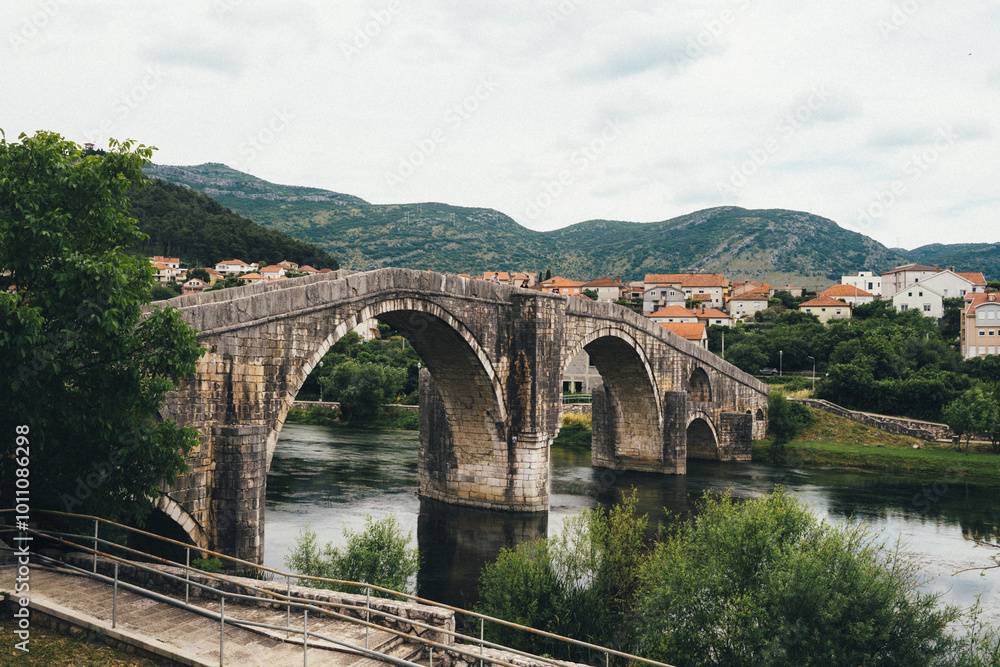 Historic Ottoman bridge over the river in Bosnia and Herzegovina surrounded by green landscapes and quaint village homes Historic Ottoman bridge over the river in Bosnia and Herzegovina surrounded by green landscapes and quaint village homes
