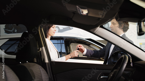 Tableau sur toile A stylish young woman enjoys her new car purchase in a modern showroom