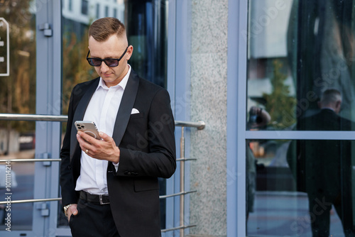 Sleek Urban Professional in Modern Attire Engaging with Smartphone Outside a Contemporary Building