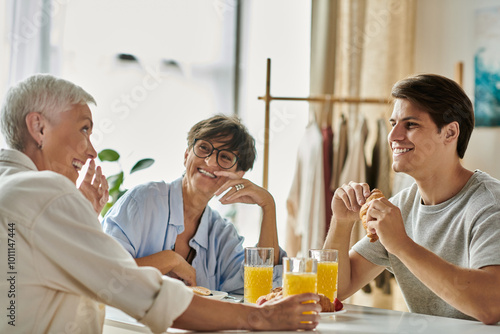 A gay couple enjoys a cheerful breakfast with their adult son, sharing laughs and delicious food.